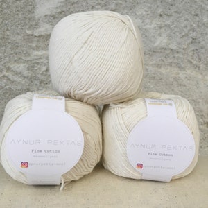 Könnte beinhalten: Drei Knäuel weißer Baumwollgarn mit Etiketten, auf denen "Aynur Pektas Fine Cotton" steht und ein Social-Media-Handle angegeben ist.