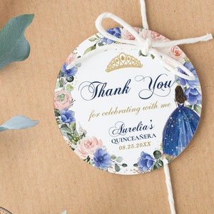 May include: Round thank you tag with a blue and white floral design, a gold crown, and a silhouette of a woman in a blue dress. The text reads "Thank You for celebrating with me Aurelia's Quinceañera 08.25.20XX".