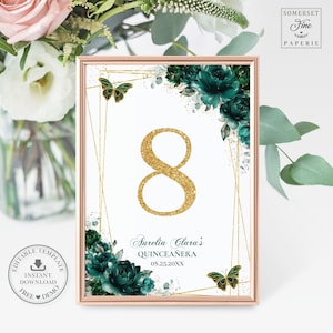 May include: Table number eight with gold glitter font and a green floral design. The text reads "Aurelia Clara's Quinceañera 08.25.20XX".