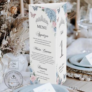 May include: A three-sided wedding menu card with floral and butterfly designs in pastel blue and pink. The menu includes appetizers, main courses, and desserts. The card has the text "MENU" and "Table 1".