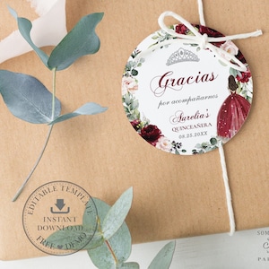 May include: Round white favor tag with a red and pink floral border. The tag features a crown, the text "Gracias por acompa&ntilde;arnos Aurelia's Quincea&ntilde;era 08.25.20XX", and a watercolor illustration of a woman in a red dress.