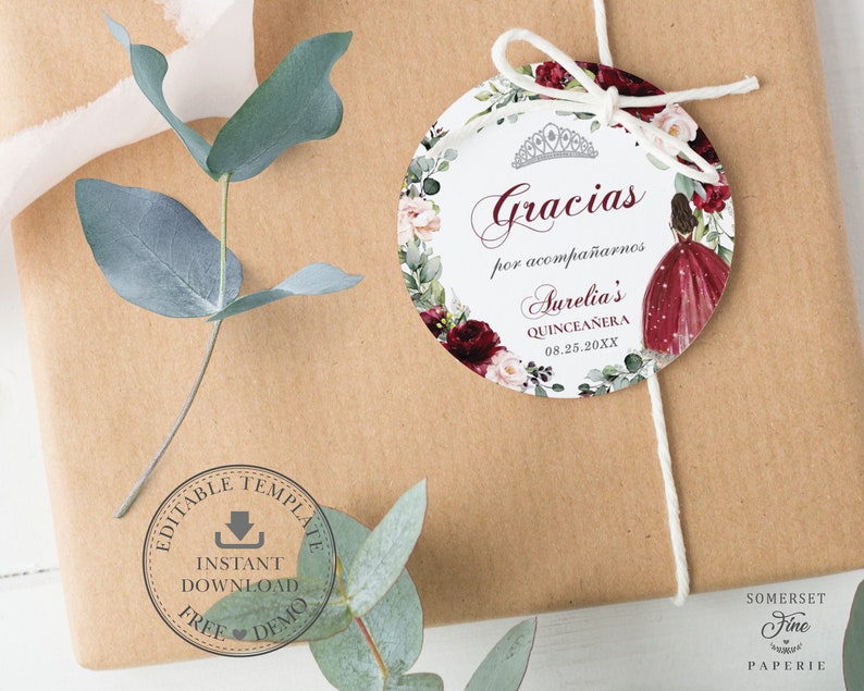 May include: Round white favor tag with a red and pink floral border. The tag features a crown, the text "Gracias por acompa&ntilde;arnos Aurelia's Quincea&ntilde;era 08.25.20XX", and a watercolor illustration of a woman in a red dress.