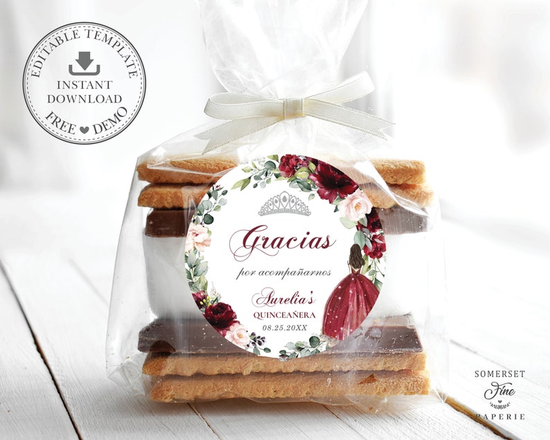 May include: A round favor tag with a floral design in shades of burgundy and white. The tag features a tiara, a girl in a burgundy dress, and the text "Gracias por acompa&ntilde;arnos Aurelia's Quincea&ntilde;era 08.25.20XX".