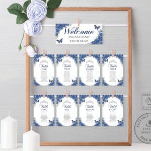 Puede incluir: Un marco de madera muestra un letrero de bienvenida y ocho tarjetas de mesa, todas con un diseño floral azul y detalles de mariposas. El letrero de bienvenida dice "Welcome, PLEASE FIND YOUR SEAT." Cada tarjeta de mesa está numerada del uno al ocho.