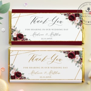 Könnte beinhalten: Zwei burgunderrote und weiße Schokoladenriegelverpackungen mit goldenen Akzenten. Die Verpackungen zeigen ein florales Design mit burgunderroten und weißen Blumen und Grün. Der Text auf den Verpackungen lautet "Vielen Dank" und "Für die Teilnahme an unserem Hochzeitstag" mit den Namen des Paares und dem Hochzeitsdatum.