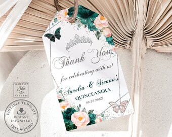 May include: A white thank you tag with a silver glitter design. The tag features a floral design with pink and green flowers, butterflies, and a silver crown. The text on the tag reads "Thank You for celebrating with us! Aurelia & Sienna's Quinceañera 08.25.20XX".