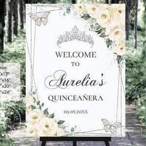 May include: A printable welcome sign for a Quinceañera, featuring a white background with a silver geometric frame, white roses, and butterflies. The text reads "Welcome to Aurelia's Quinceañera 09.08.20XX".