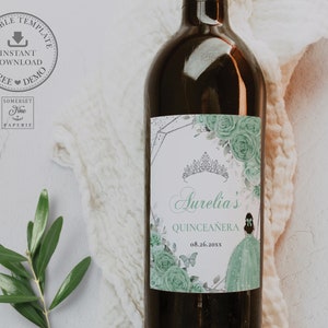 May include: A green and silver wine bottle label with a floral design and a crown. The label says "Aurelia's Quinceañera 08.26.20XX".