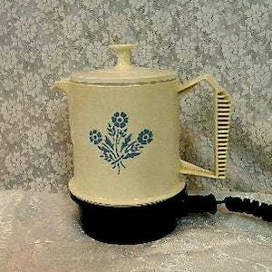 May include: Cream-colored electric coffee pot with a black base and handle. The pot features a blue floral design and a matching lid. A black power cord extends from the base.
