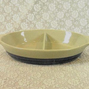 May include: Oval ceramic serving dish with a divided interior. The dish has a light tan upper section and a dark blue lower section. It features handles on either side and is suitable for serving appetizers or side dishes.