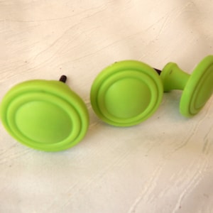 Könnte beinhalten: Drei limegrüne Schrankknöpfe mit einem erhabenen, konzentrischen Kreisdesign. Die Knöpfe haben einen einfachen, modernen Stil.