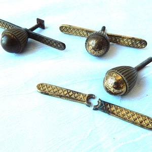 Op de afbeelding: Drie antieke messing kastknoppen met een decoratief eikelontwerp. De knoppen hebben een platte, rechthoekige basis met een ruitpatroon.