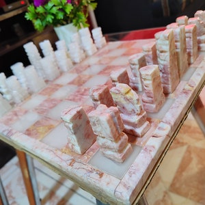 Pu&ograve; includere: Un set di scacchi in marmo con pezzi bianchi e rosa su una scacchiera in marmo rosa e bianco.