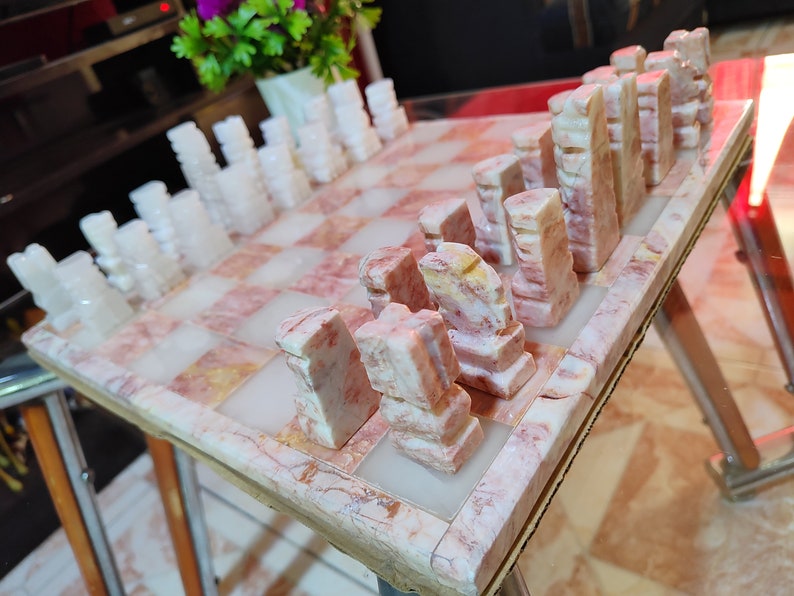 Pu&ograve; includere: Un set di scacchi in marmo con pezzi bianchi e rosa su una scacchiera in marmo rosa e bianco.