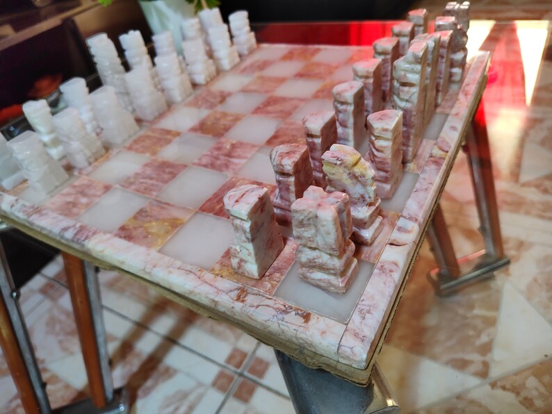 Pu&ograve; includere: Un set di scacchi in marmo con pezzi rosa e bianchi su una scacchiera in marmo rosa e bianco.