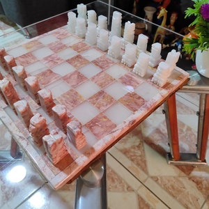 Pu&ograve; includere: Un set di scacchi in marmo rosa e bianco con pezzi degli scacchi bianchi su una scacchiera in marmo rosa e bianco.