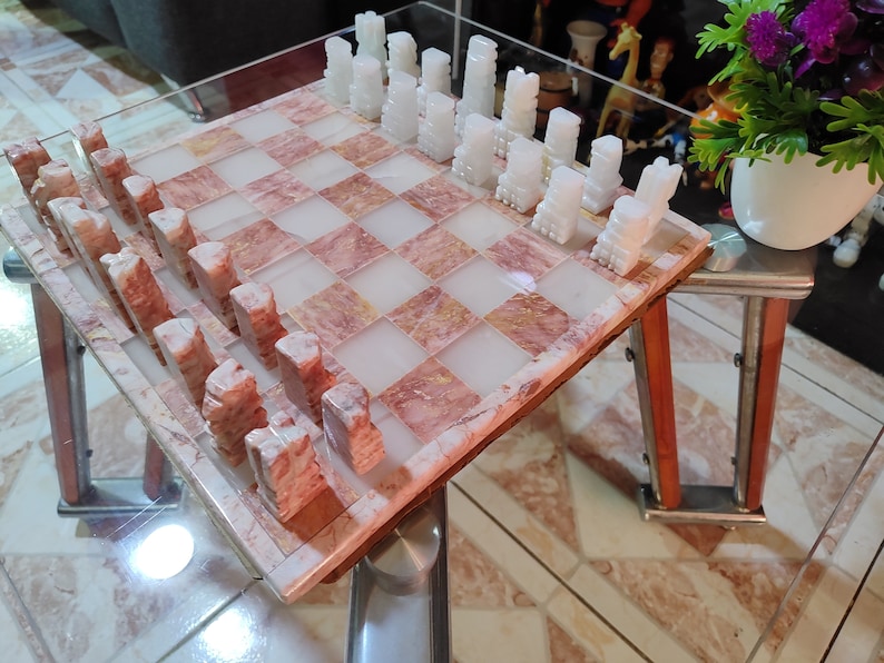 Pu&ograve; includere: Un set di scacchi in marmo rosa e bianco con pezzi degli scacchi bianchi su una scacchiera in marmo rosa e bianco.