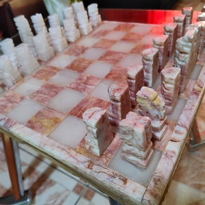 Pu&ograve; includere: Un set di scacchi in marmo con pezzi bianchi e rosa su una scacchiera in marmo rosa e bianco.