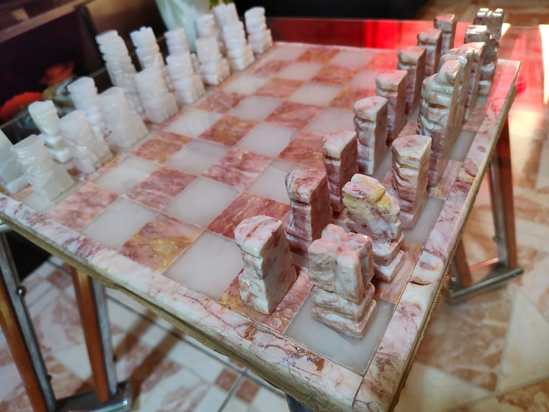 Pu&ograve; includere: Un set di scacchi in marmo con pezzi bianchi e rosa su una scacchiera in marmo rosa e bianco.