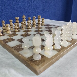 May include: A marble chess set with white and brown pieces on a brown and white marble chessboard.