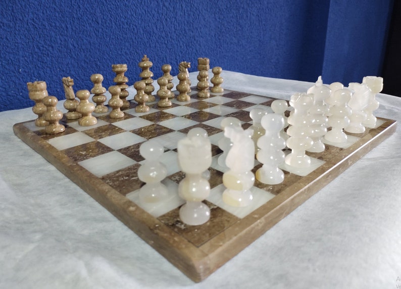 May include: A marble chess set with white and brown pieces on a brown and white marble chessboard.
