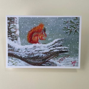 May include: A red squirrel perched on a snow-covered branch in a winter woodland scene. The squirrel is looking to the right, and the background is a soft blue with falling snow.