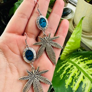 May include: A pair of silver dangle earrings with a blue abalone shell and a silver marijuana leaf charm.