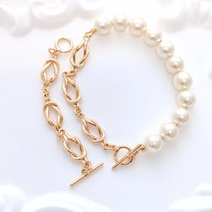 May include: A gold-toned bracelet and matching necklace set. The necklace features a series of gold knot-shaped links. The bracelet is made of large, round, cream-colored pearls. Both pieces have gold clasps.