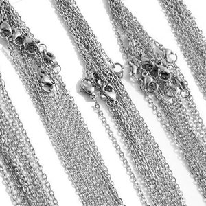 May include: A collection of silver chain necklaces of varying lengths and thicknesses. The chains are arranged in a fan shape, with the ends of the chains overlapping.
