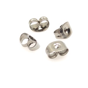 May include: Four silver earring backs, also known as earring stoppers, are shown against a white background. The earring backs are designed to secure earrings to the earlobe.