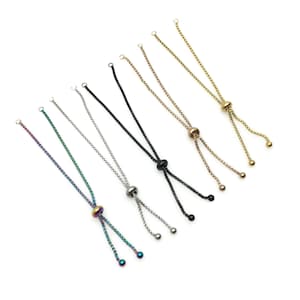 May include: Assortment of seven adjustable bracelet cords in various colors, including black, silver, gold, and iridescent. Each cord features a small bead at the end and a larger bead in the center.