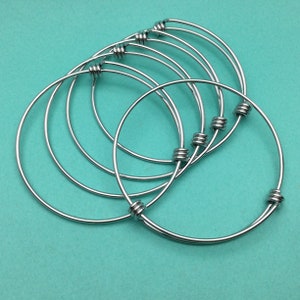 May include: Set of six silver bangle bracelets with a knotted design. The bracelets are stacked on top of each other.