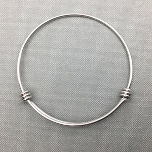 May include: A silver bangle bracelet with a simple design. The bracelet is made of a thin, round wire and has two small, round clasps on either side.