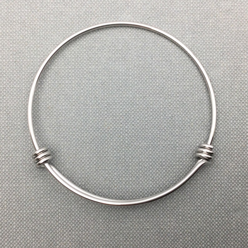 May include: A silver bangle bracelet with a simple design. The bracelet is made of a thin, round wire and has two small, round clasps on either side.