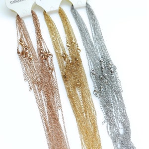 May include: A set of three gold, rose gold, and silver chain necklaces. The chains are all the same style, but in different colors. They are hanging from a white background.