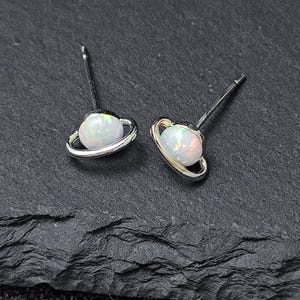 May include: A pair of silver earrings with a white opal gemstone set in a ring that resembles a planet with rings.