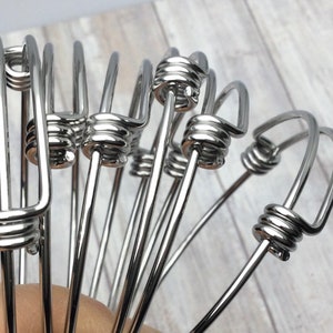 May include: A close-up of a group of silver bangle bracelets with a twisted wire design. The bracelets are stacked on top of each other and are made of a shiny metal.