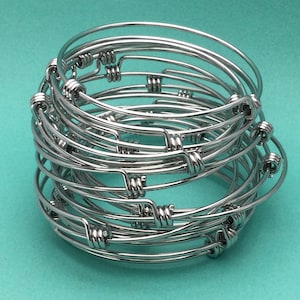 May include: A stack of silver bangle bracelets with a twisted design. The bracelets are stacked on top of each other, creating a layered effect.