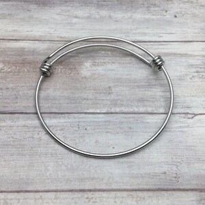 May include: A silver expandable bangle bracelet with a simple design. The bracelet is made of metal and has a smooth finish.