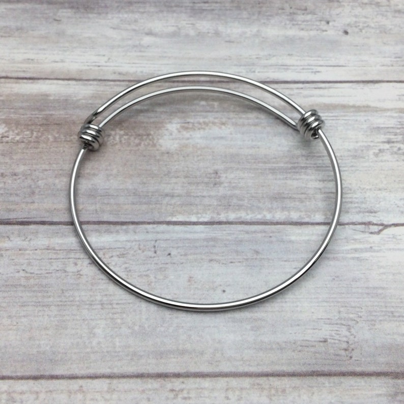 May include: A silver expandable bangle bracelet with a simple design. The bracelet is made of metal and has a smooth finish.