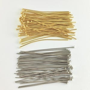 以下が含まれることがあります： ジュエリー作りのためのヘッドピンの2つの山。上の山は金色で、下の山は銀色です。