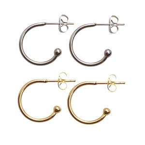 May include: A pair of silver hoop earrings and a pair of gold hoop earrings. Each earring has a small ball at the end of the hoop.