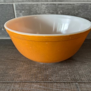 May include: A vintage yellow mixing bowl with a white interior. The bowl is made of glass and has a smooth, rounded shape.
