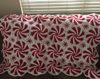 May include: A white and red crocheted throw blanket with a peppermint swirl design.
