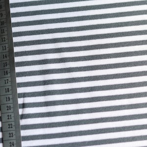 Könnte beinhalten: Nahaufnahme von weiß-grau gestreiftem Stoff mit einem Maßband am linken Rand. Das Band misst von 8 bis 24 Zoll.
