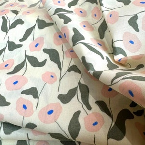 Könnte beinhalten: Ein weißer Stoff mit einem sich wiederholenden Muster aus rosa Blüten und grünen Blättern. Der Stoff ist gefaltet und drapiert, wodurch das Muster aus verschiedenen Blickwinkeln sichtbar wird.