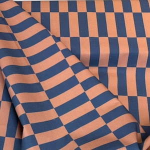 Könnte beinhalten: Ein gefalteter Stoff mit einem sich wiederholenden Muster aus abwechselnd marineblauen und rostfarbenen Rechtecken. Der Stoff ist drapiert, wodurch Falten und Schatten entstehen, die dem Design Tiefe verleihen. Das Muster ist ein klassisches, geometrisches Design.