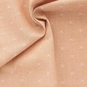 Könnte beinhalten: Nahaufnahme eines pfirsichfarbenen Stoffes mit einem weißen Kreuzstichmuster. Der Stoff ist gefaltet und hat einen goldenen Saum entlang der Kante. Der Text "Fableism" ist in der unteren rechten Ecke sichtbar.