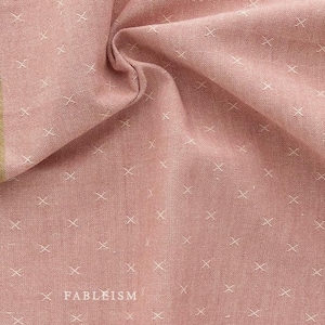 Könnte beinhalten: Nahaufnahme eines rosa Stoffes mit einem weißen Kreuzstichmuster. Der Stoff hat eine subtile Textur und eine weiche, gedämpfte rosa Farbe. Der Stoff ist gefaltet und drapiert, wodurch seine Falten und Textur sichtbar werden.