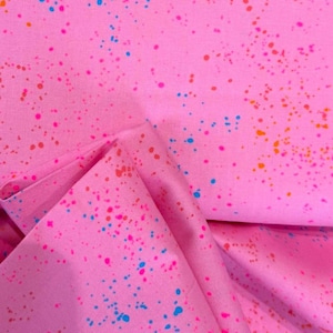 Könnte beinhalten: Rosa Stoff mit einem Spritzmuster in Rosa-, Orange- und Blautönen. Der Stoff ist gefaltet und zeigt die Textur und Farbvariationen des Materials. Das Gesamtthema ist verspielt und farbenfroh.